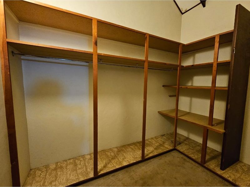 A walk-in closet or storage area featuring built-in wooden shelving units and hanging rails, providing functional storage space.