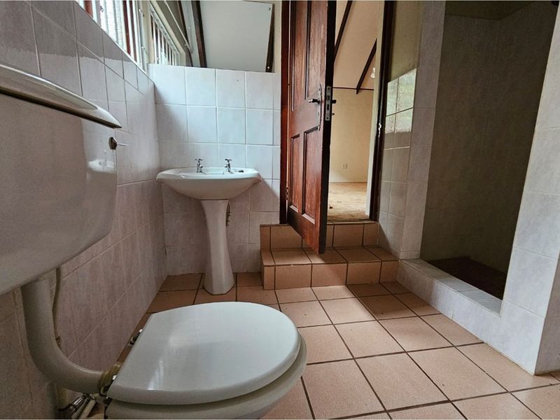 A dated bathroom featuring a pedestal basin, toilet, and walk-in shower area with tiled flooring and walls, requiring modernization.