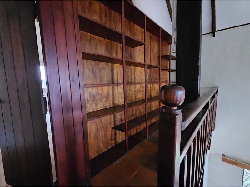 A hallway landing featuring extensive built-in timber shelving and a traditional wooden balustrade, showcasing classic cottage architectural character.