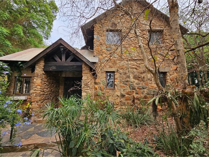 A charming two-story stone cottage featuring rustic masonry, timber gable detailing, and leaded glass windows, set within a lush, established garden environment.
