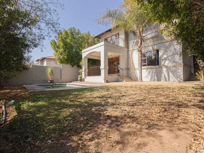 Rear view of the property featuring a swimming pool, covered patio, and upper-level balcony set within a private garden area.