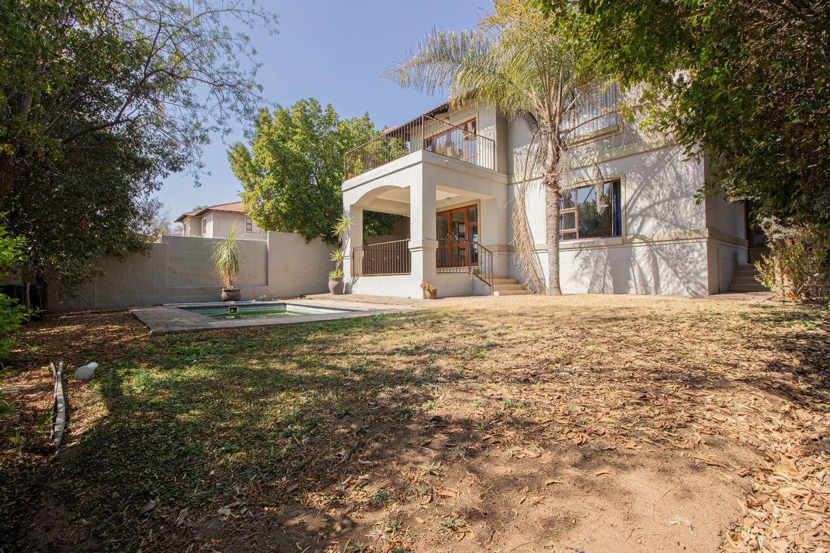 Rear view of the property featuring a swimming pool, covered patio, and upper-level balcony set within a private garden area.