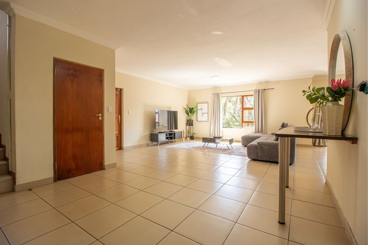 Spacious living room featuring neutral tiled flooring, coving, and natural light through a large window, providing a comfortable and versatile living space.
