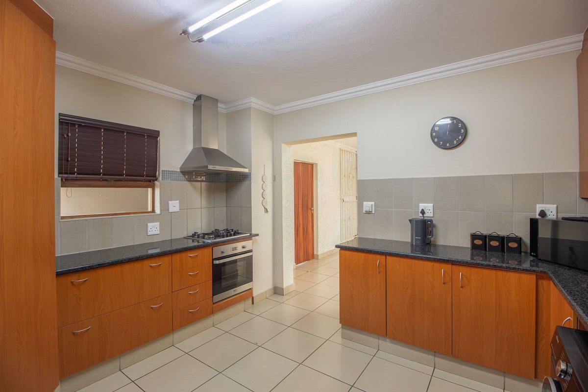 Functional kitchen featuring wood-finish cabinetry, granite countertops, a gas hob, built-in oven, and tiled flooring with a neutral backsplash.