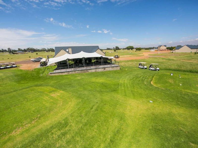 Aerial view of a clubhouse building situated on a golf course, featuring a large paved patio area and expansive surrounding green space.