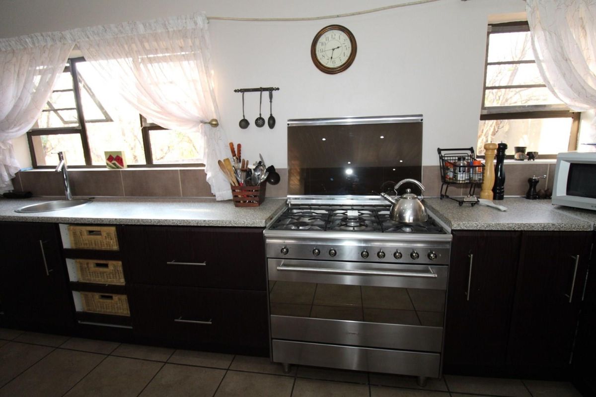 A functional kitchen featuring dark cabinetry, a stainless steel gas stove with extractor, tiled flooring, and a double sink with tiled splashbacks.