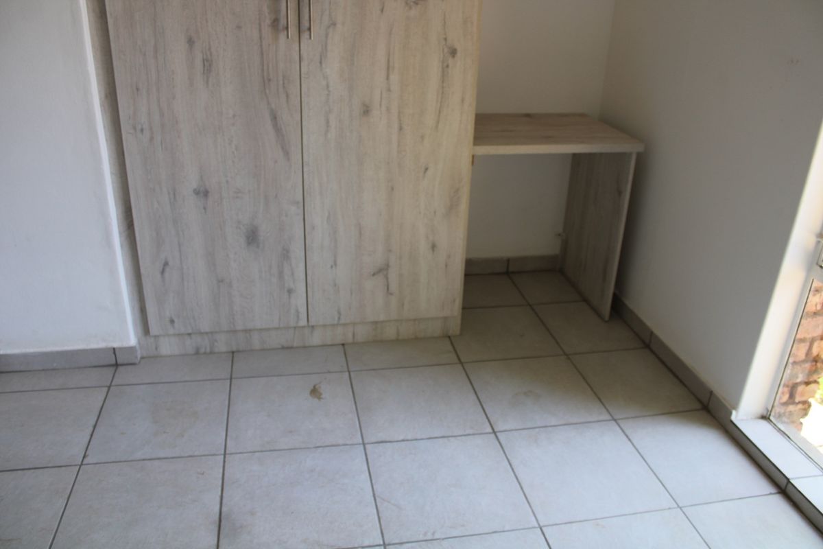 A bedroom featuring built-in light wood-grain cabinetry with an integrated desk area and neutral ceramic floor tiling.