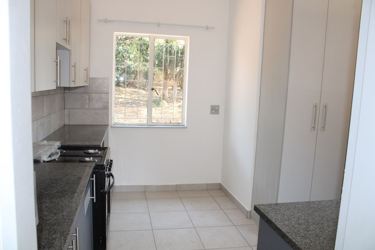 A functional kitchen featuring granite countertops, built-in cabinetry, tiled flooring, and a window overlooking the garden area.