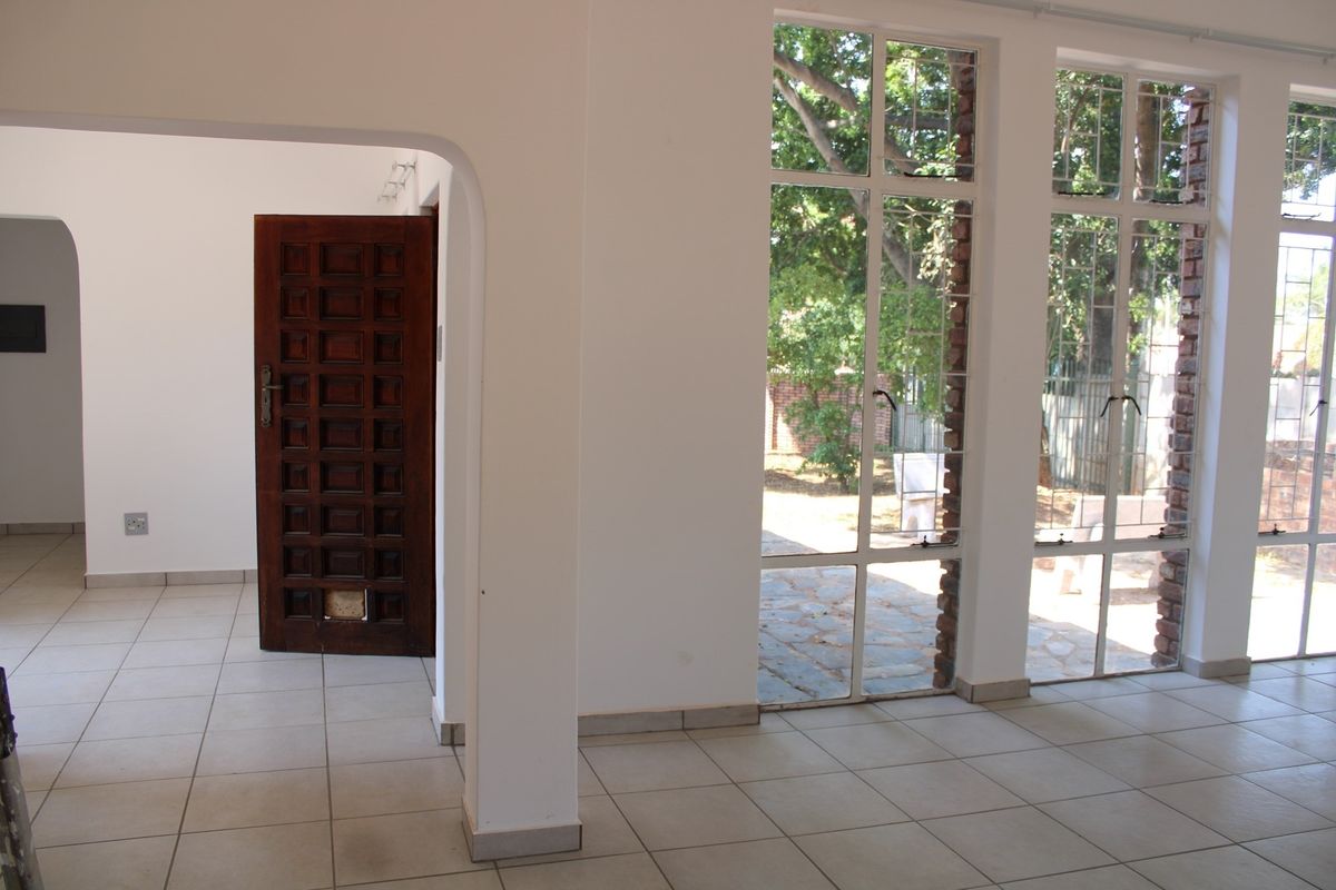 Bright living area featuring large steel-framed windows, tiled flooring, and a classic wooden door leading to an adjacent room.