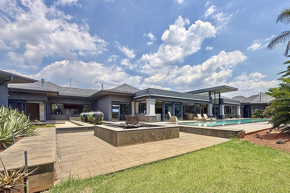 Spacious rear exterior featuring a modern swimming pool, expansive paved patio area, water feature, and seamless indoor-outdoor flow through large sliding glass doors.