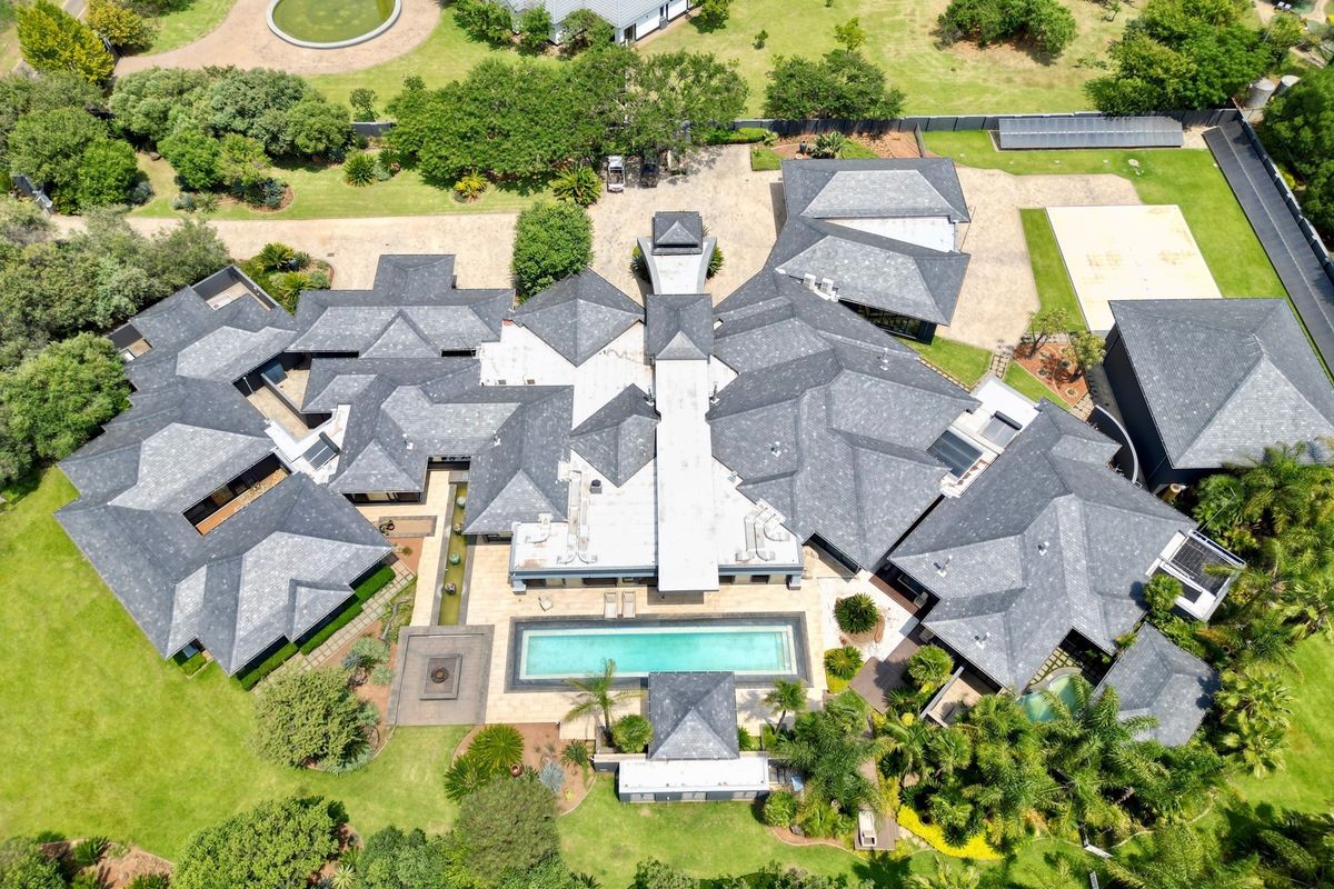 Aerial view of a large luxury residence featuring an extensive slate roof, a central swimming pool, and expansive landscaped grounds.