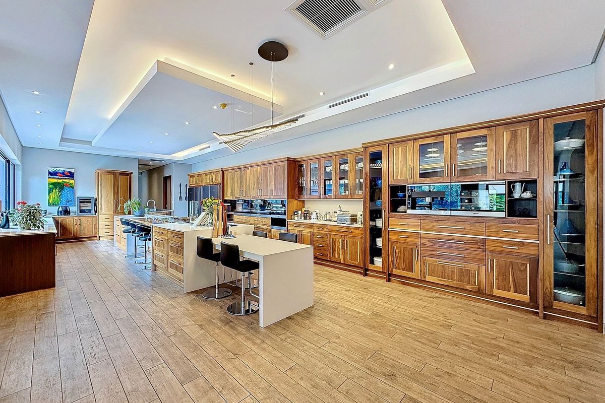 Spacious modern kitchen featuring extensive timber cabinetry, stone island benchtop, integrated appliances, and recessed ceiling lighting with high-quality finishes.