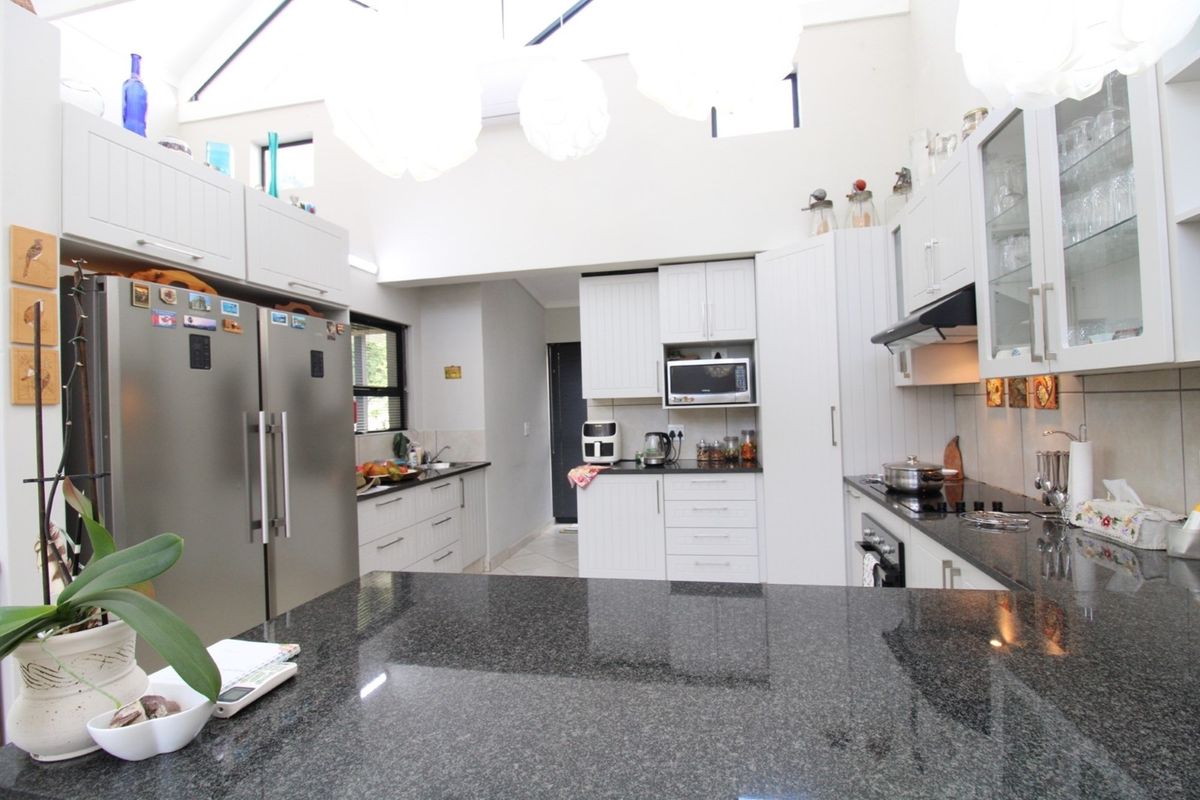 A bright, spacious kitchen featuring white cabinetry, dark granite countertops, a built-in oven, hob, and extractor fan, with high ceilings and natural light.