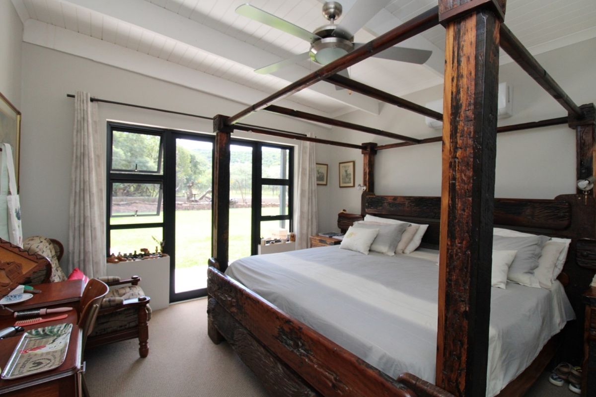 A spacious bedroom featuring a vaulted ceiling with exposed beams, a ceiling fan, and large windows with direct access to the garden.