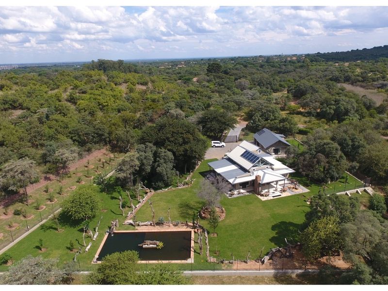 Aerial view of a spacious property featuring a main residence with solar panels, a secondary building, a swimming pool, and extensive landscaped grounds.