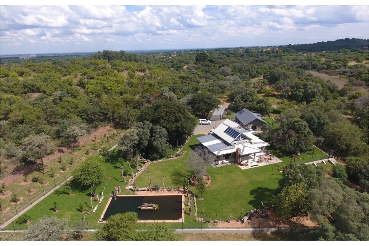 Aerial view of a spacious property featuring a main residence with solar panels, a secondary building, a swimming pool, and extensive landscaped grounds.
