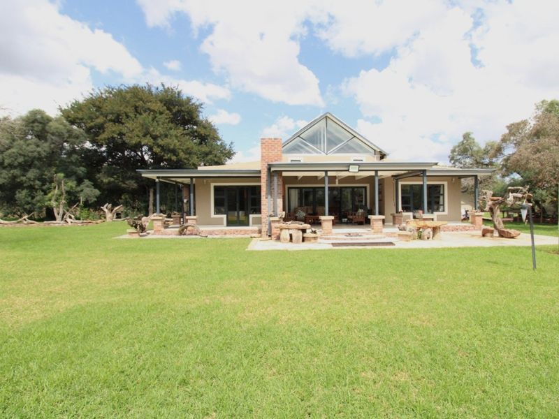 Rear view of the house featuring a covered patio, brick chimney, and large triangular gable window overlooking a spacious green lawn.