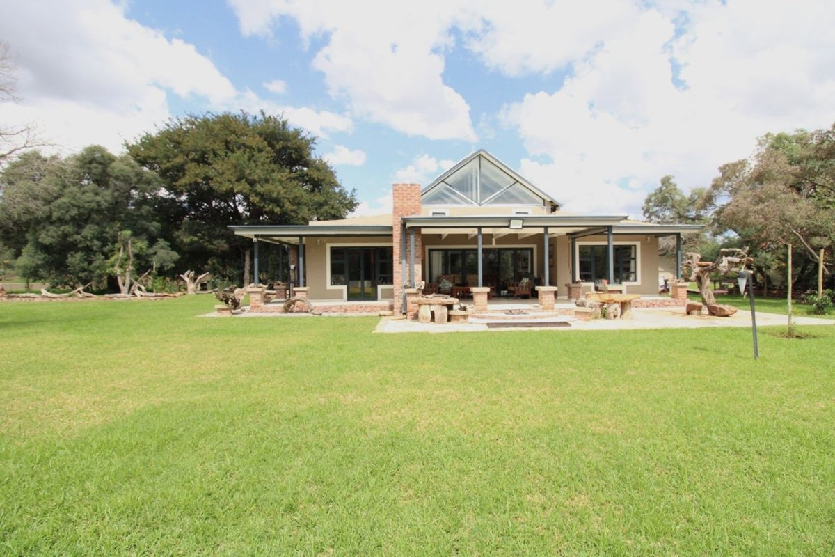 Rear view of the house featuring a covered patio, brick chimney, and large triangular gable window overlooking a spacious green lawn.