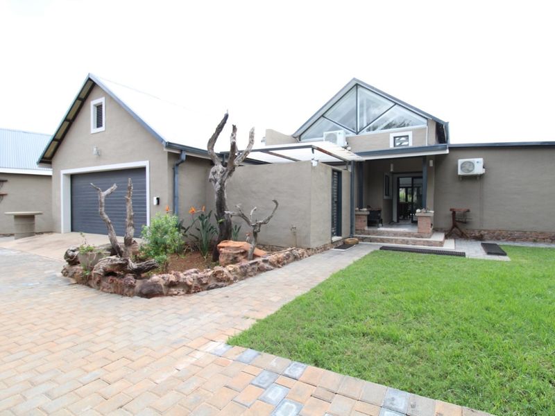 Front exterior view of the house featuring a paved driveway, garage, landscaped garden bed, and a covered entrance with modern architectural roof detailing.