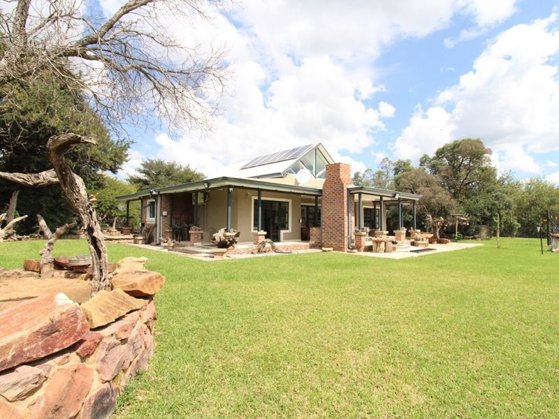 A rear view of the house featuring a covered patio, brick chimney, and solar panels set within a spacious, well-maintained garden.