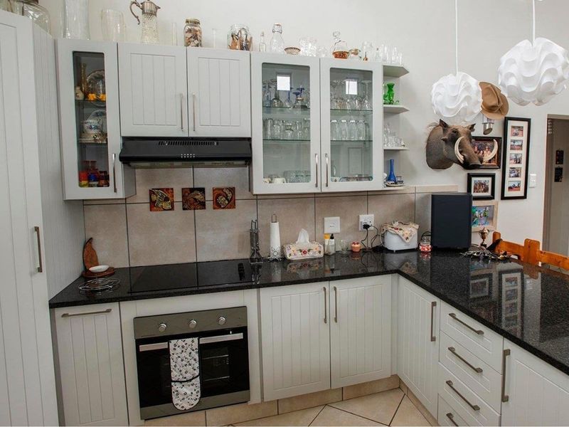 A well-maintained kitchen featuring white cabinetry, dark granite countertops, a built-in oven, and a glass-top hob with an integrated extractor fan.