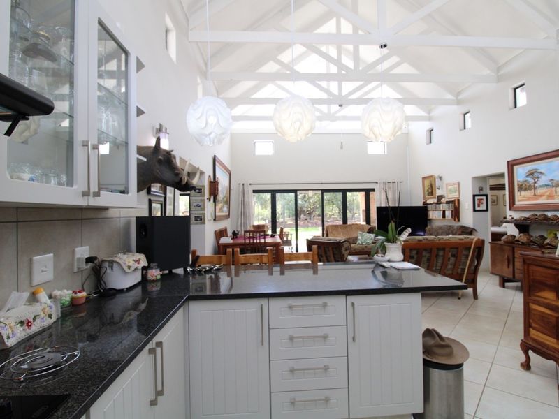 Spacious open-plan kitchen and living area featuring high vaulted ceilings with exposed trusses, granite countertops, and large sliding doors leading to the outdoor space.