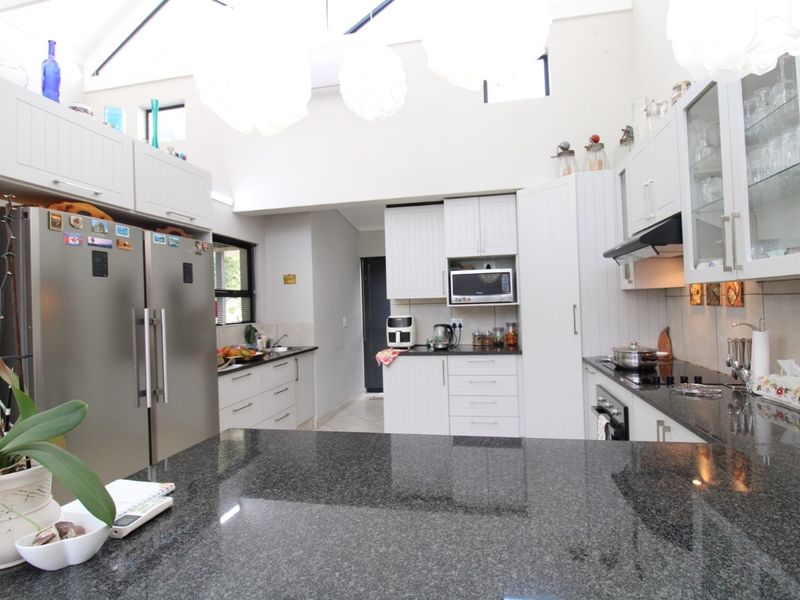 A bright, spacious kitchen featuring white cabinetry, dark granite countertops, a built-in oven, hob, and extractor fan, with high ceilings and natural light.