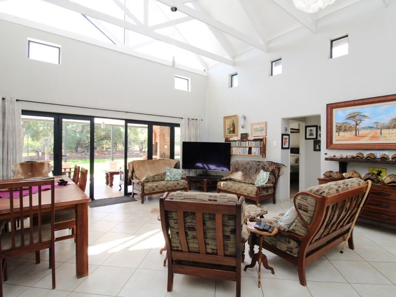 Spacious open-plan living and dining area featuring high vaulted ceilings, exposed trusses, tiled flooring, and large sliding doors opening to the outdoor patio.