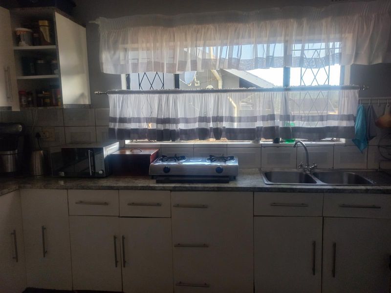 Functional kitchen featuring white cabinetry, laminate countertops, a stainless steel double sink, and a built-in gas hob with tiled backsplash.