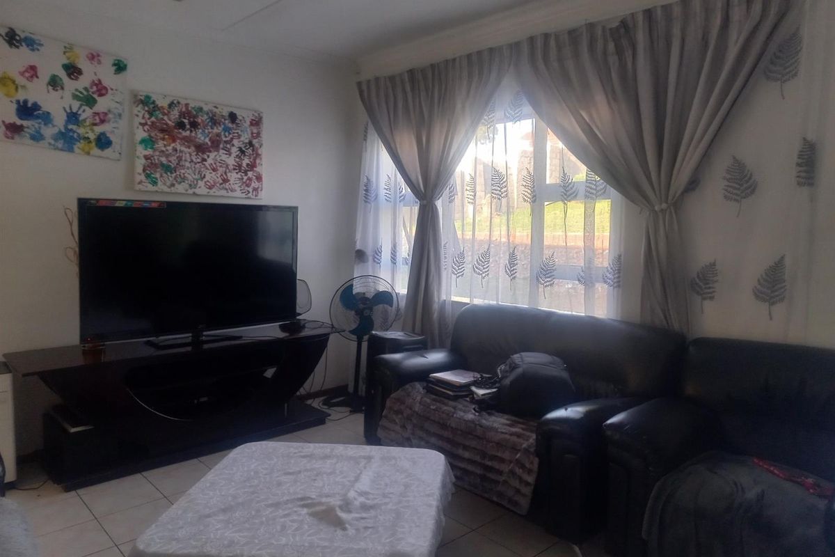 A living room featuring tiled flooring and a large window with curtains, providing natural light to the space.
