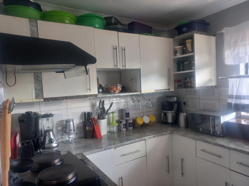 A functional kitchen featuring white built-in cabinetry, laminate countertops, a tiled backsplash, and an integrated extractor fan with an electric hob.