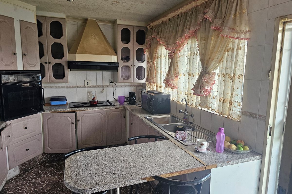 A dated kitchen featuring built-in cabinetry, a hob, extractor fan, and double sink with tiled finishes throughout.