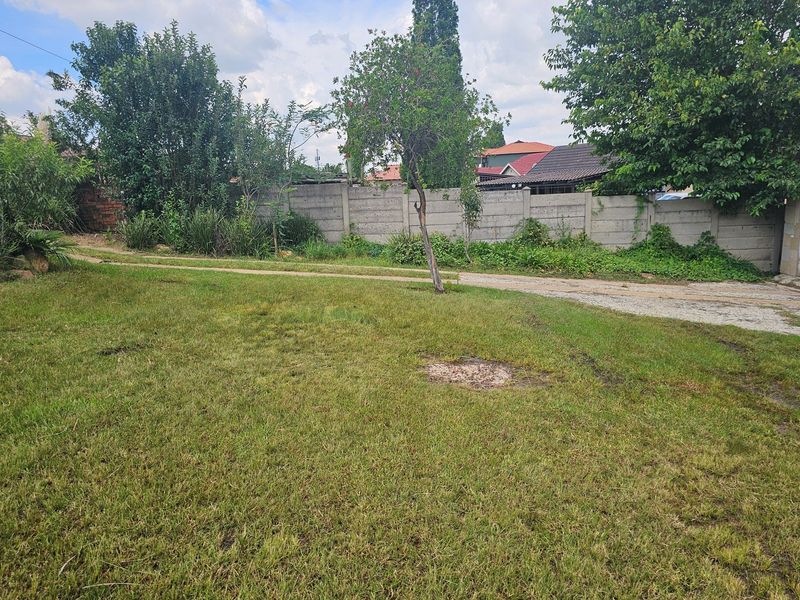 A spacious backyard area featuring a large lawn, established trees, and a precast concrete boundary wall.