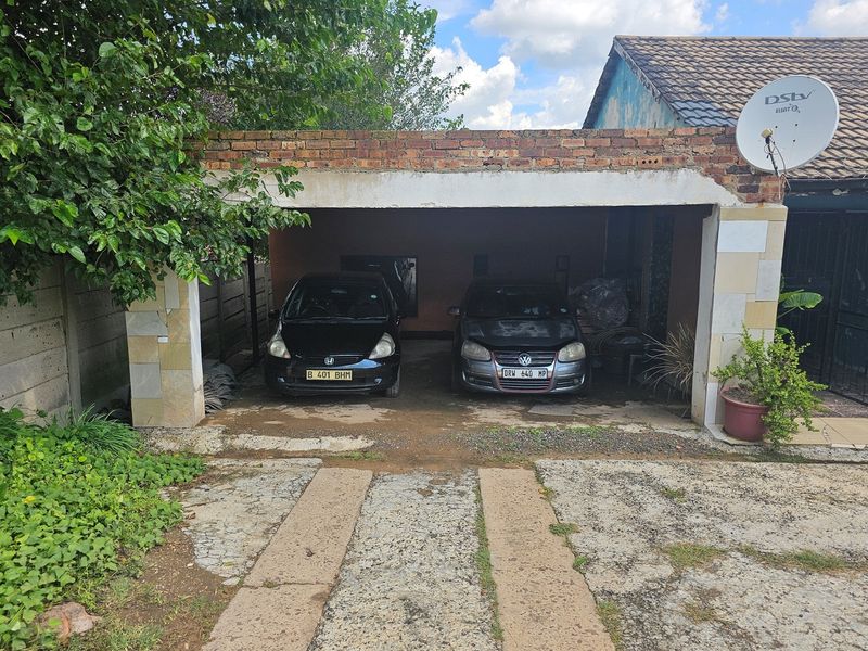 A double carport structure with a brick facade and concrete driveway, showing signs of wear and weathering.