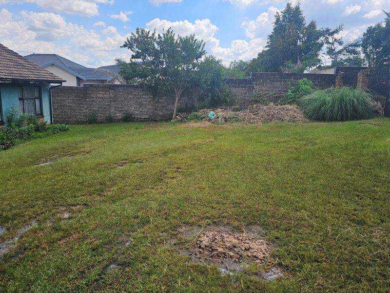 A spacious rear garden featuring a large lawn area enclosed by a perimeter boundary wall, requiring landscaping and maintenance.