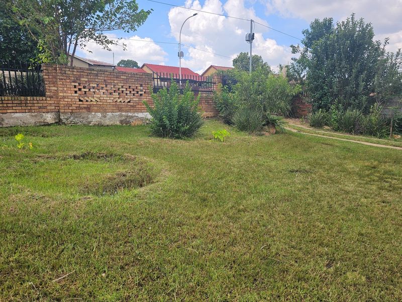 A spacious garden area featuring a brick boundary wall with integrated metal security fencing and established lawn.