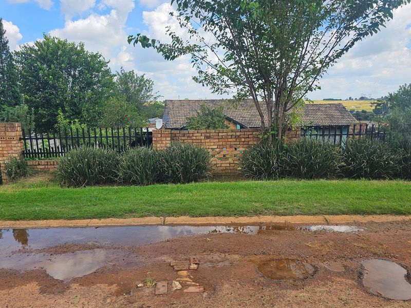 Street view of the property showing a brick boundary wall, metal security fencing, and a tiled roof visible behind mature trees.