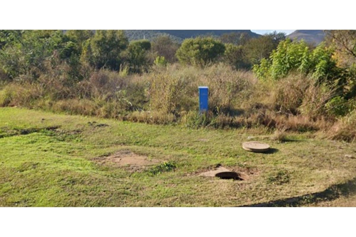 A view of the vacant residential land featuring natural vegetation, a utility connection box, and visible manhole covers on the site.