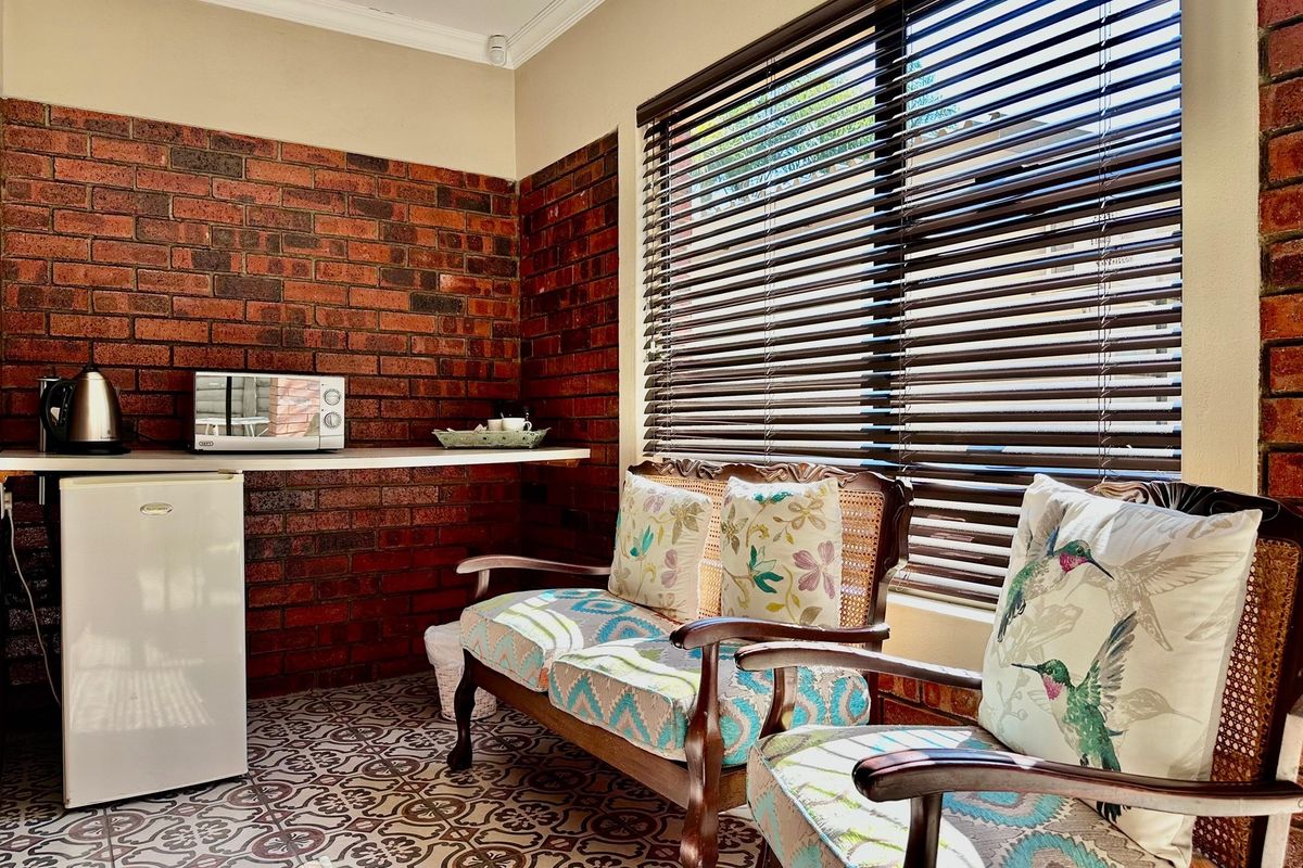 A cozy sunroom or breakfast nook featuring exposed brick walls, patterned floor tiles, and large windows with fitted venetian blinds.