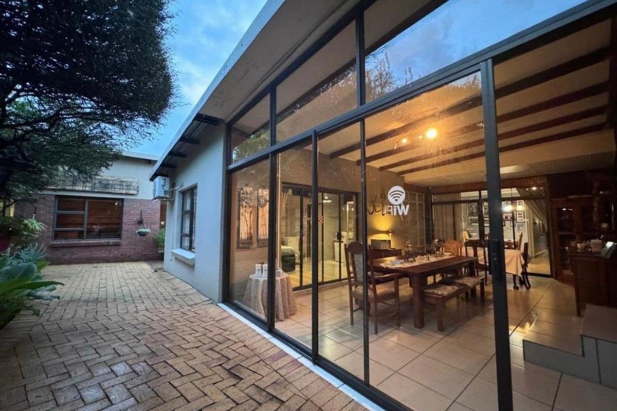 A view of the rear exterior featuring a paved courtyard and a large glass-enclosed patio area with tiled flooring.