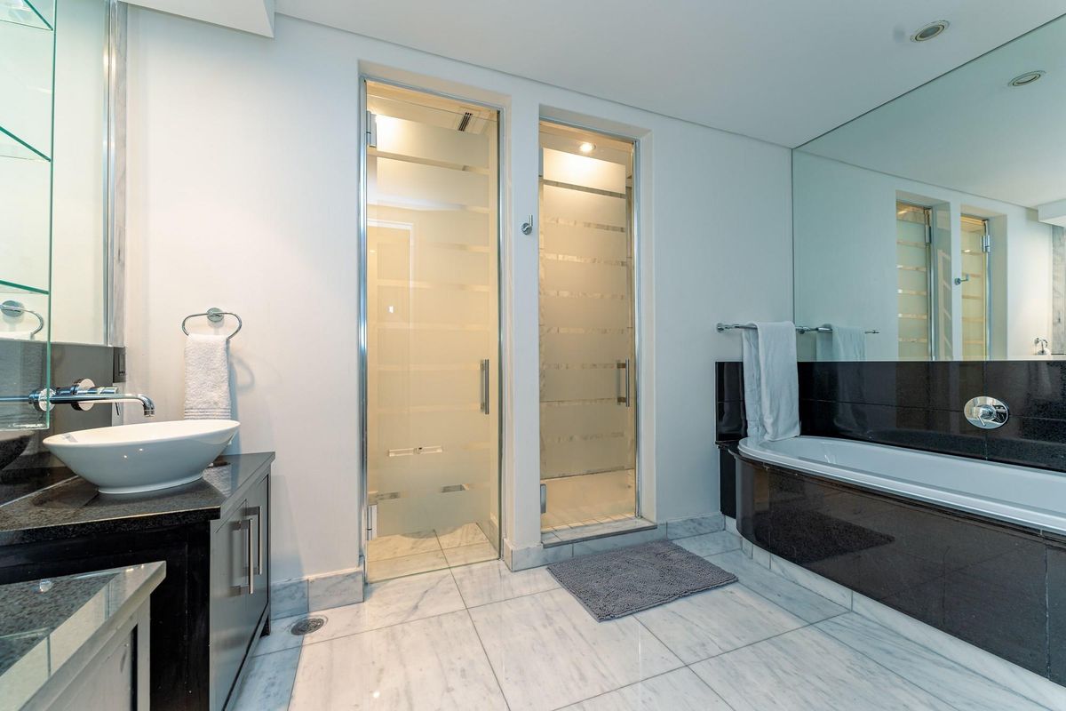Modern bathroom featuring a vessel sink, granite vanity, built-in bathtub with black surround, and two glass-enclosed shower or utility stalls.
