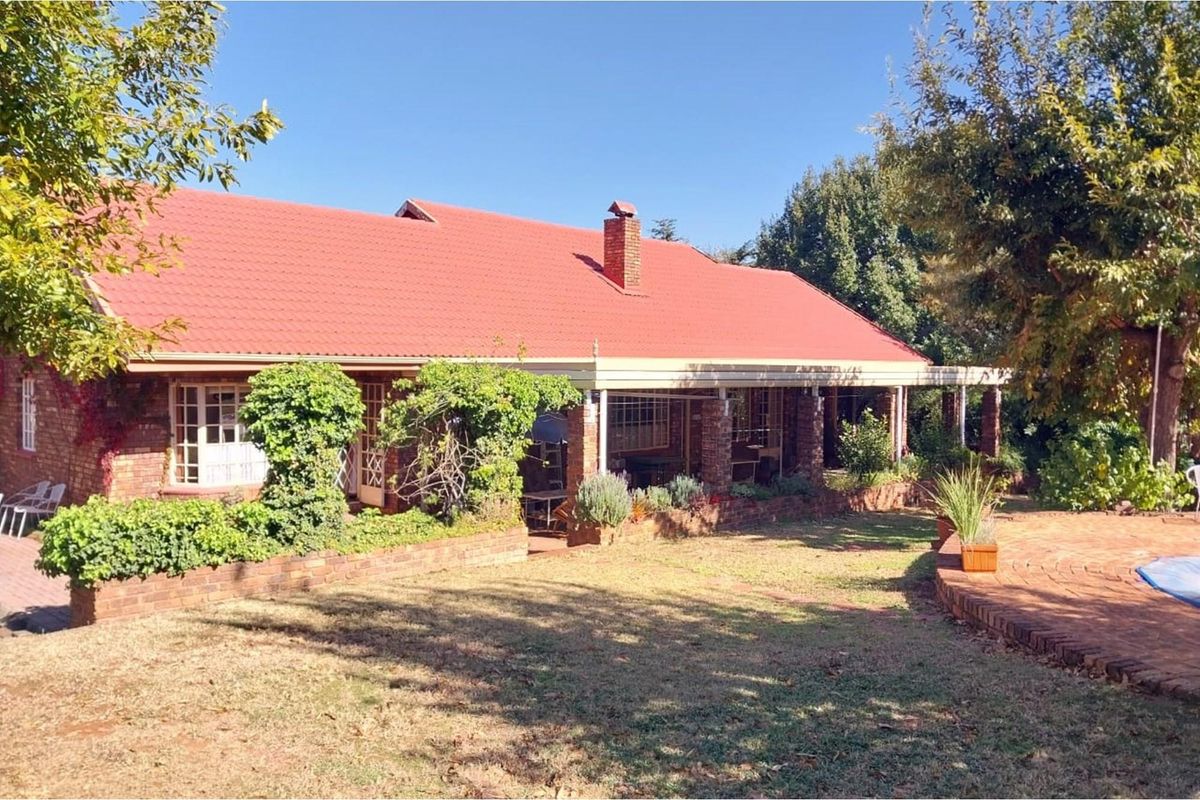 A rear view of a brick farmhouse featuring a red tiled roof, a brick chimney, and a covered patio area overlooking the garden and pool.