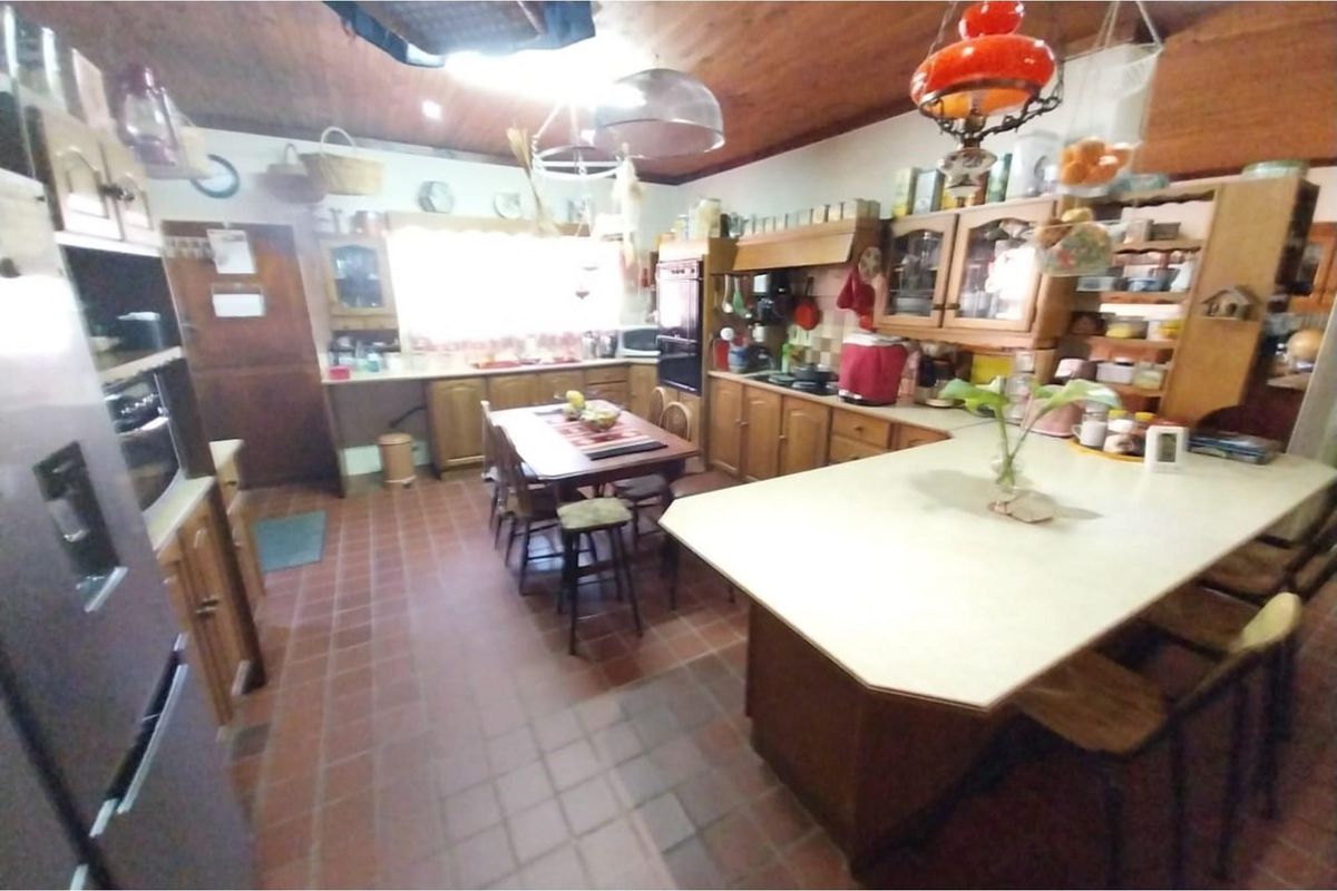 Spacious kitchen featuring wooden cabinetry, a central island with breakfast bar, and terracotta floor tiles under a timber-clad ceiling.