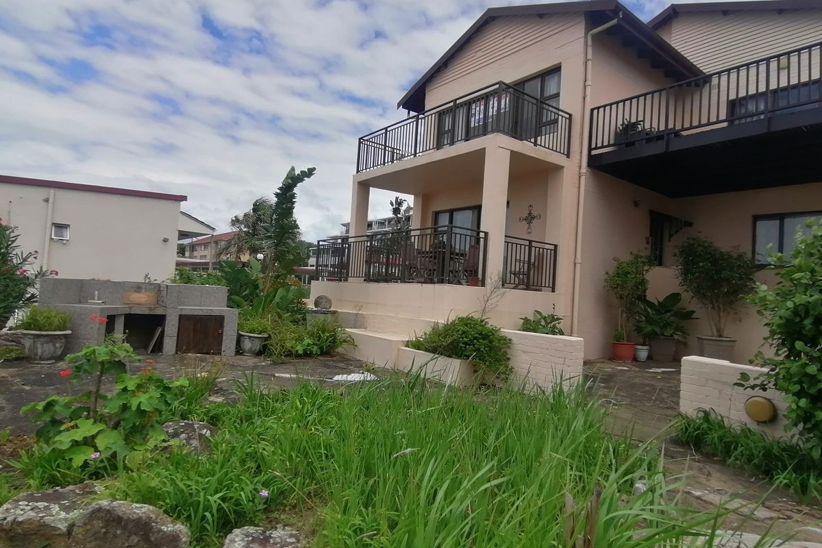 Rear view of a townhouse featuring a multi-level balcony, paved patio area, and a built-in brick braai, set within a garden space.
