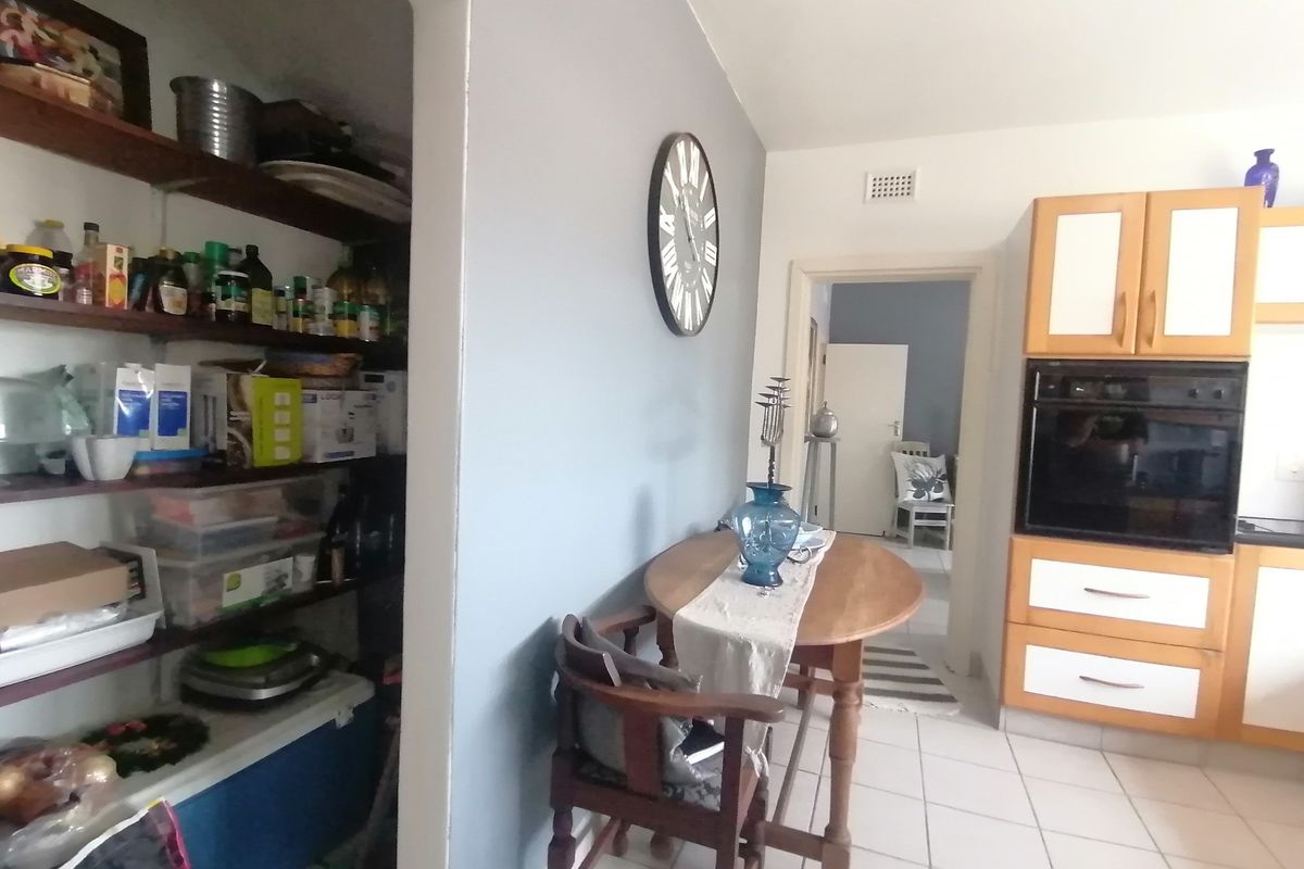 A kitchen area featuring built-in cabinetry, an integrated oven, and an adjacent walk-in pantry with open shelving, leading to a hallway.