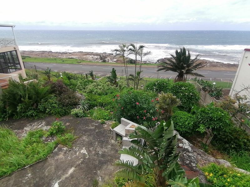 Elevated coastal view overlooking the ocean, featuring a landscaped garden and a built-in stone seating area.