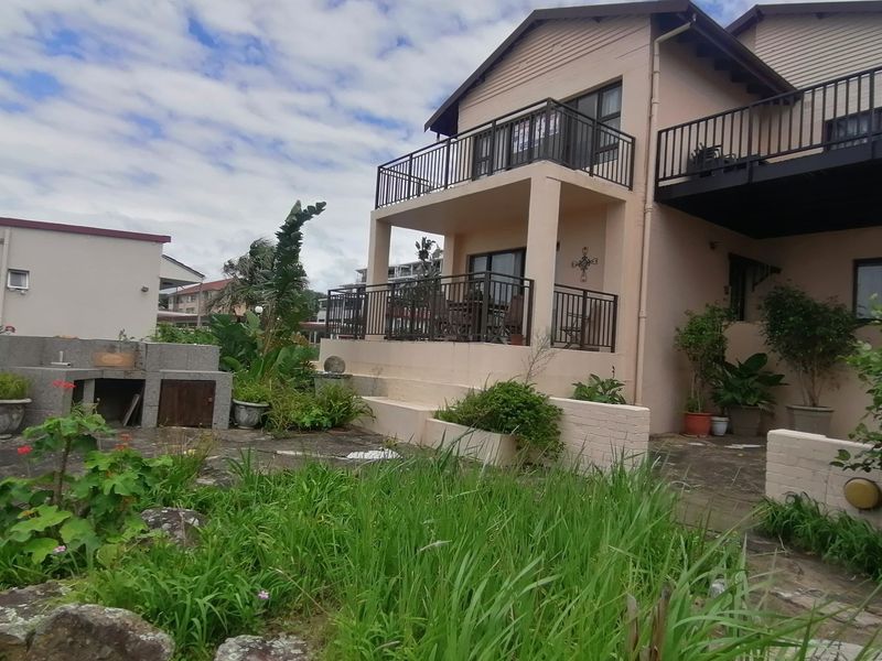 Rear exterior view of the townhouse featuring a paved patio area, built-in braai, and upper-level balcony with metal railings.