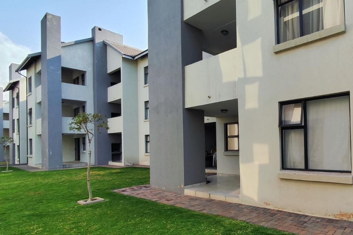 Exterior view of a modern apartment complex featuring multi-story residential blocks, private balconies, and well-maintained communal garden areas with paved walkways.