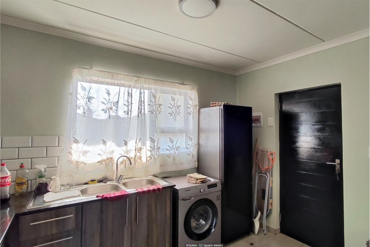 Functional kitchen area featuring a double basin sink, tiled backsplash, and dedicated space for laundry appliances.