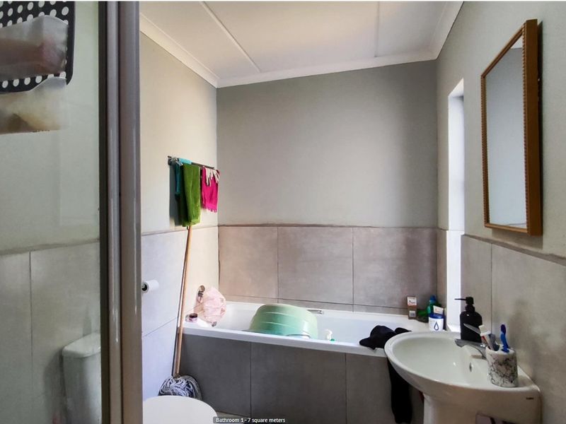 A functional bathroom featuring a built-in bathtub with tiled surround, a pedestal basin, and a toilet.